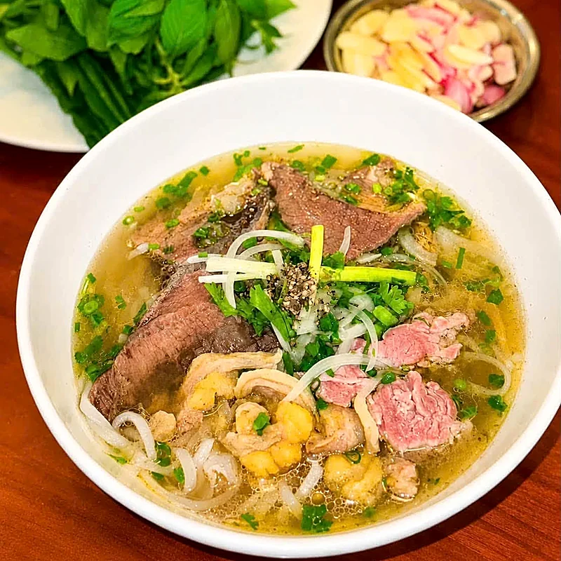 Tô phở bò tái nạm nước dùng trong, ăn kèm rau quế, sa tế và hành ngâm — thành phẩm khoá Phở Bò